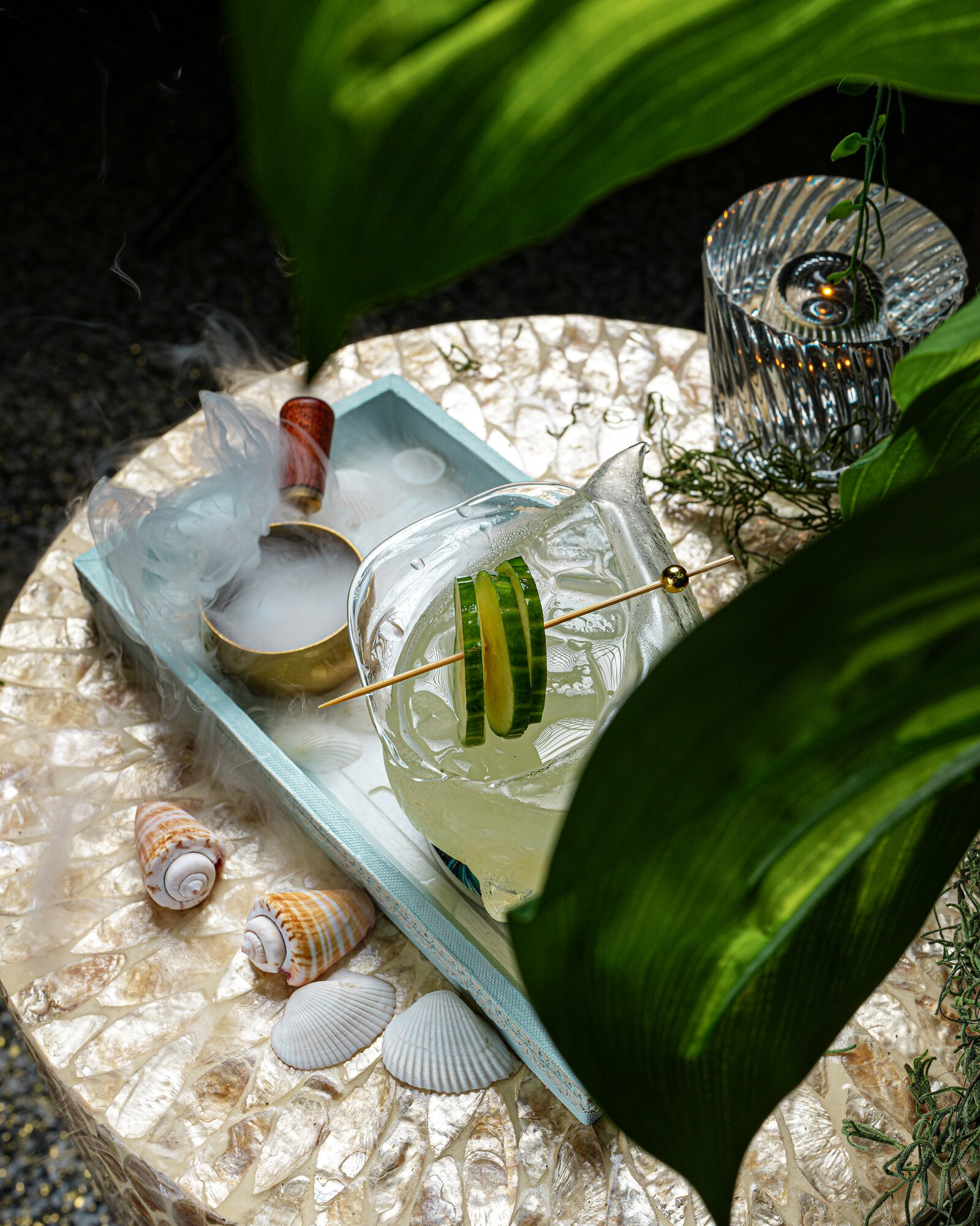A smoking cucumber cocktail styled among tropical greenery