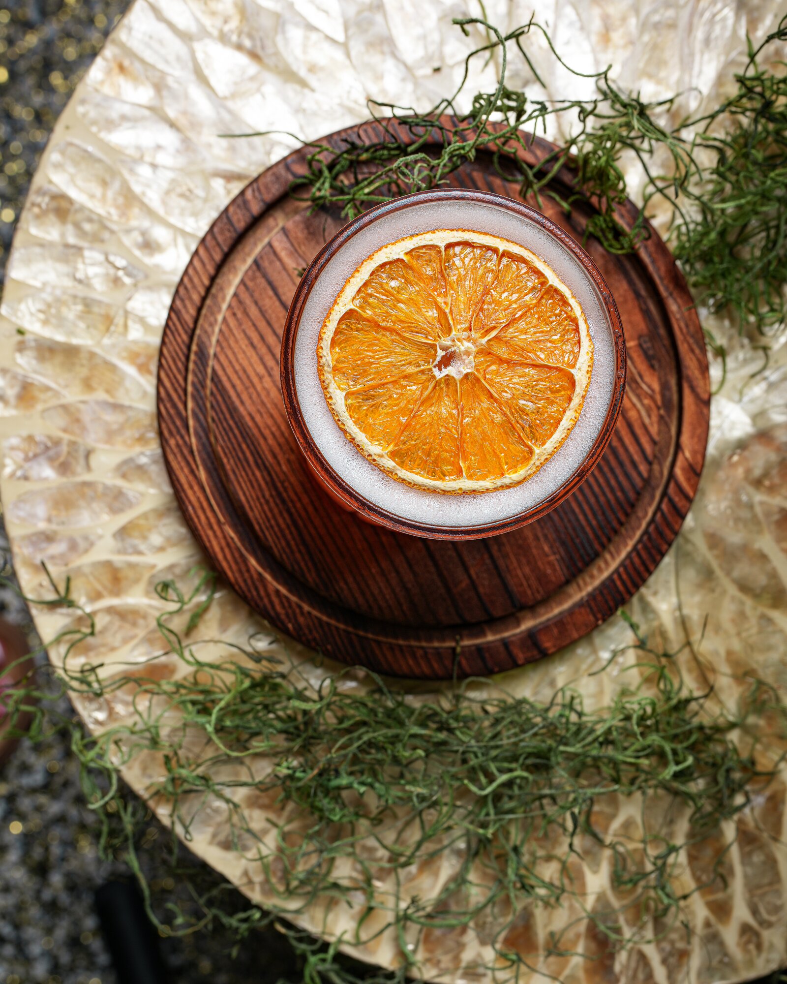 Overhead view of a foamy cocktail crowned with a dried orange slice